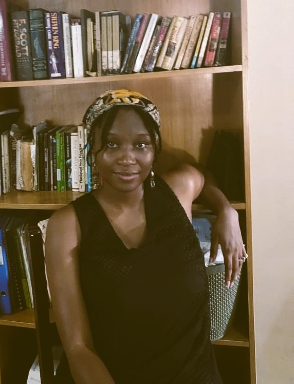 Amina Waya sitting in front of her bookshelf at home.